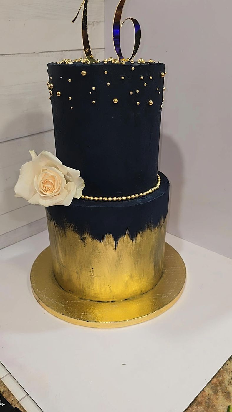 Black and gold two-tier cake with a cream rose and a number 16 topper