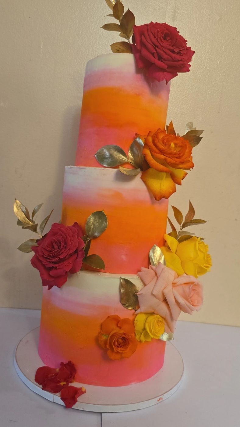 Three-tier orange and pink ombre cake decorated with red and orange roses