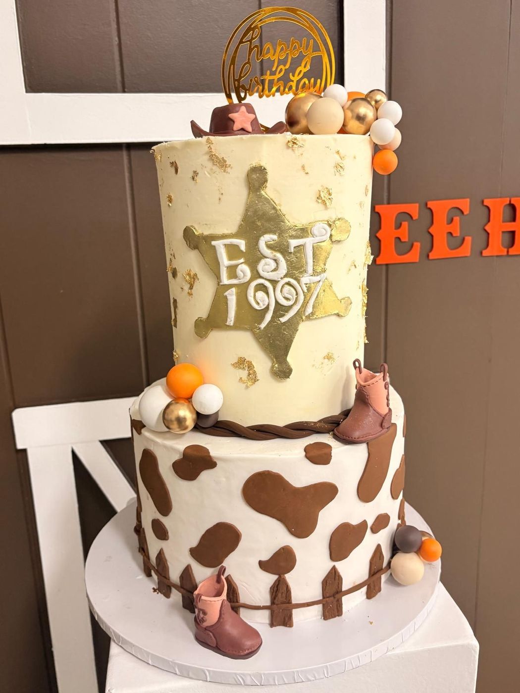 Cowboy-themed two-tier cake with cow print, fondant boots and a sheriff star