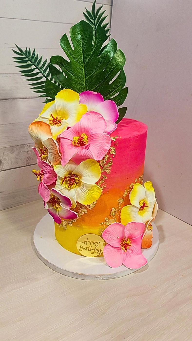 Tropical pink and yellow cake with hibiscus flowers and palm leaves