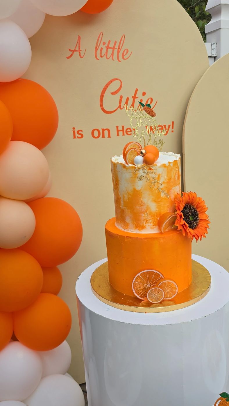 Orange and white two-tier baby shower cake with sunflower and citrus slices