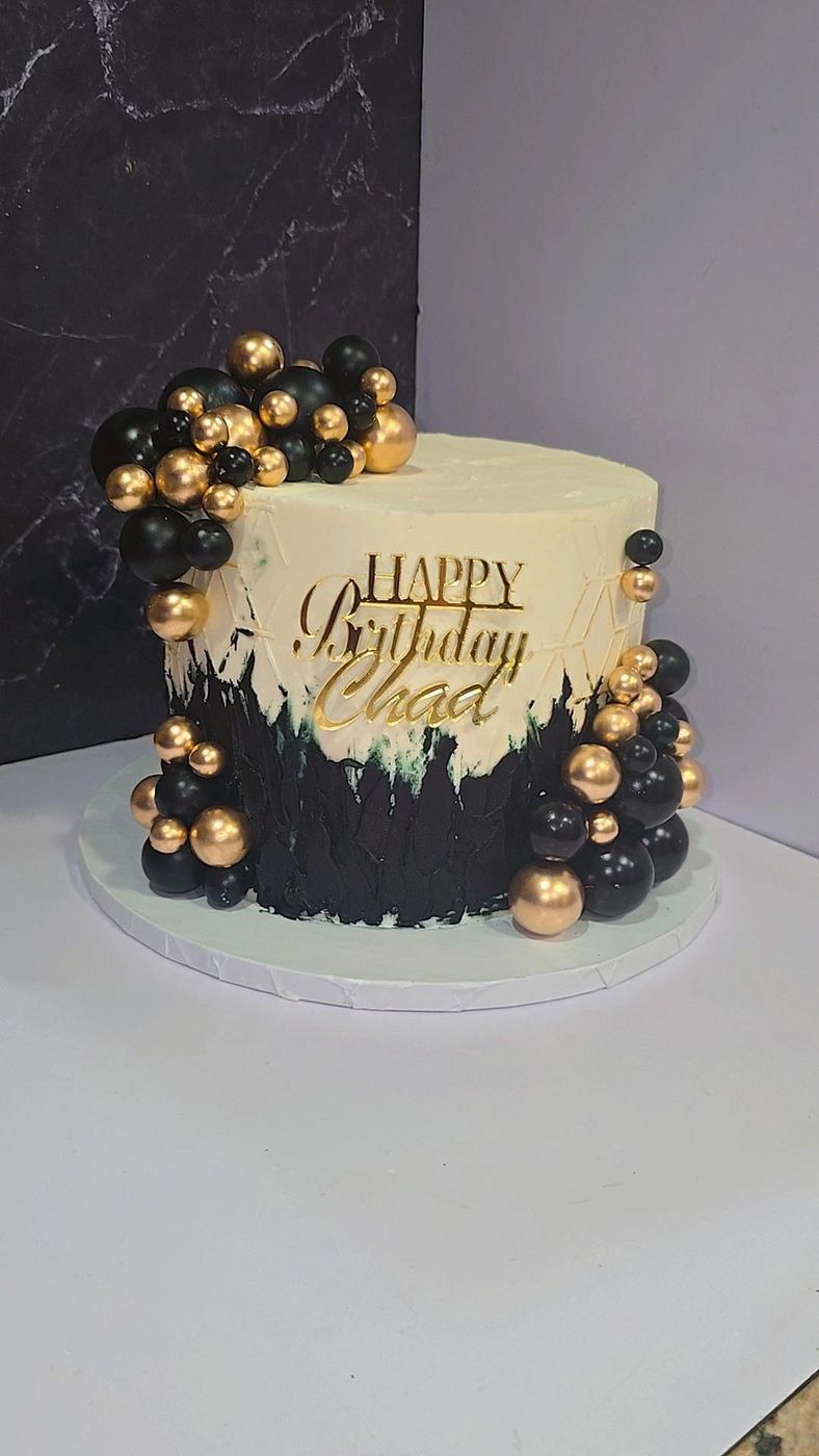 Black and gold birthday cake with gold spheres and a custom topper