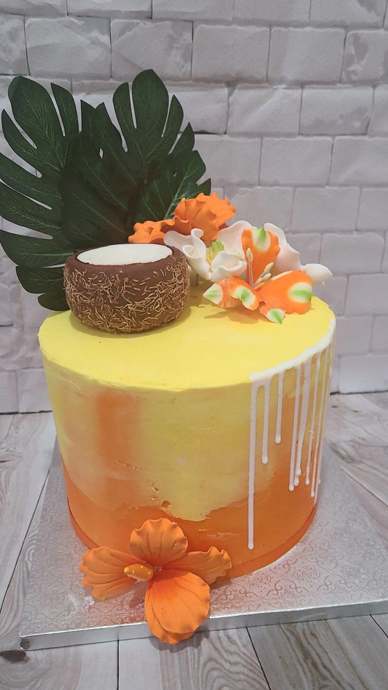 Yellow and orange tropical drip cake with a coconut and hibiscus