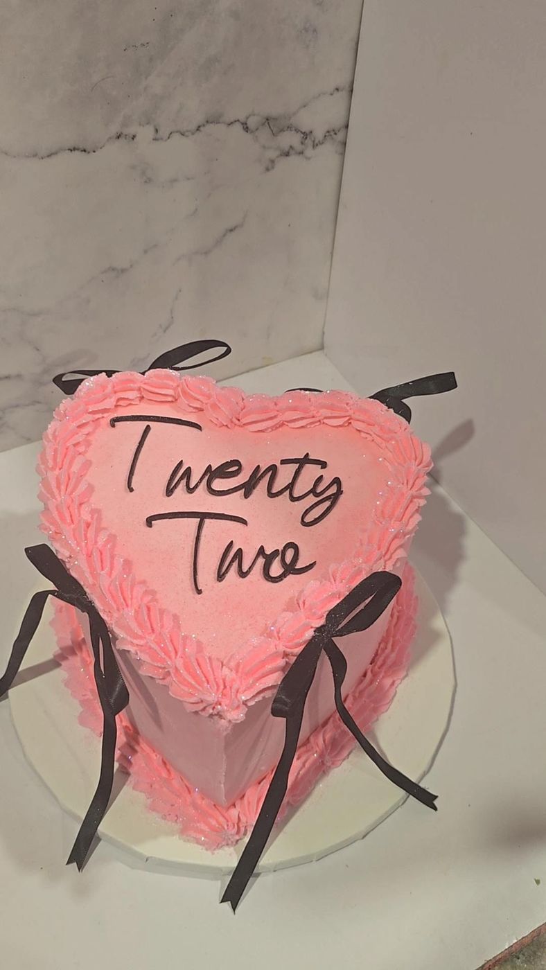 Pink heart-shaped cake with black bows and script lettering