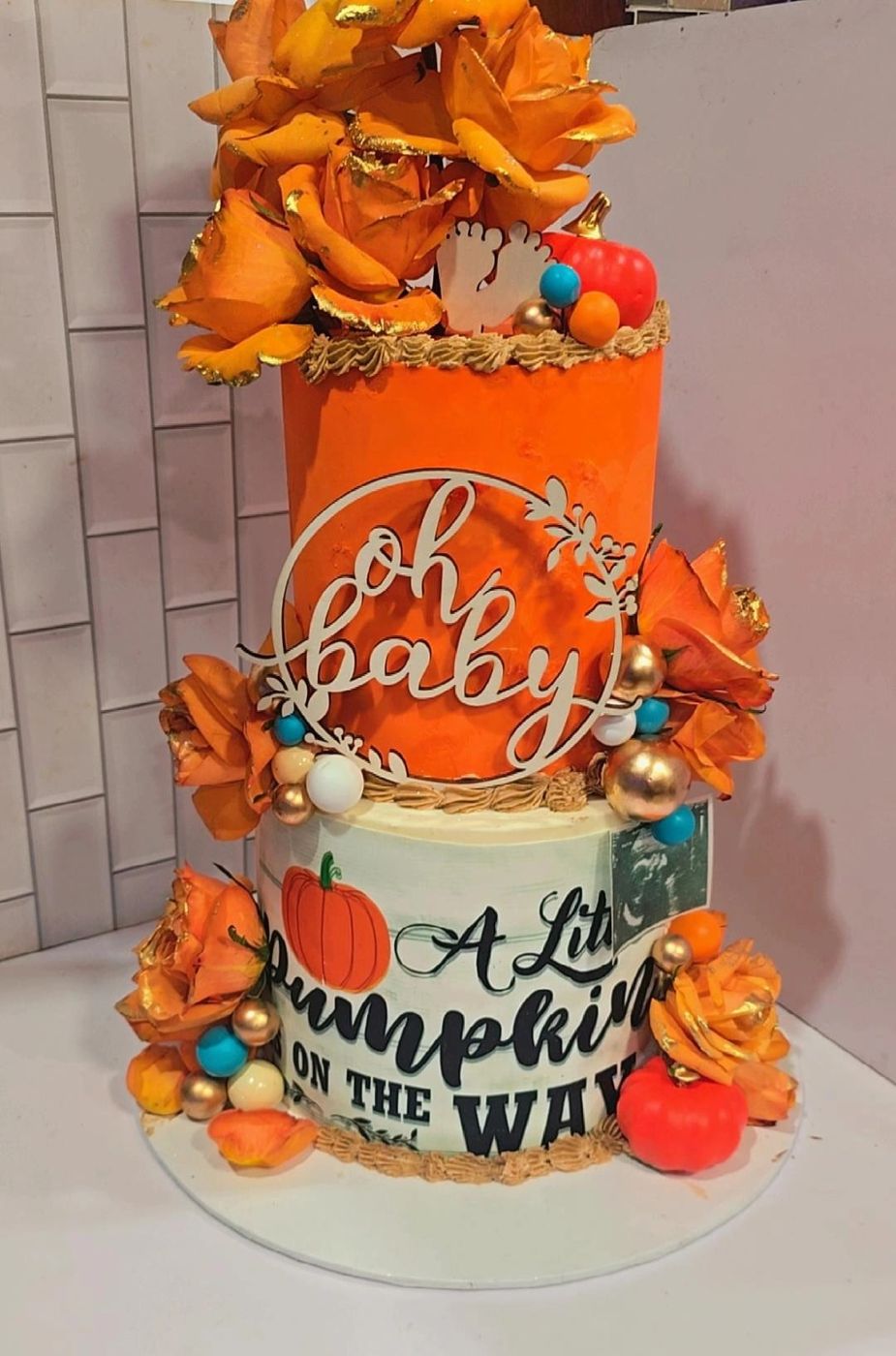 Orange two-tier baby shower cake with pumpkins and sugar flowers